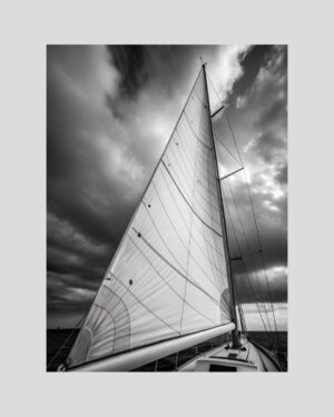 Affiche en noir et blanc d’un voilier vu du pont, voile gonflée sous un ciel nuageux